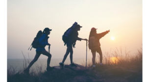 Three hikers silhouetted against a vibrant sunrise on a mountain trail.